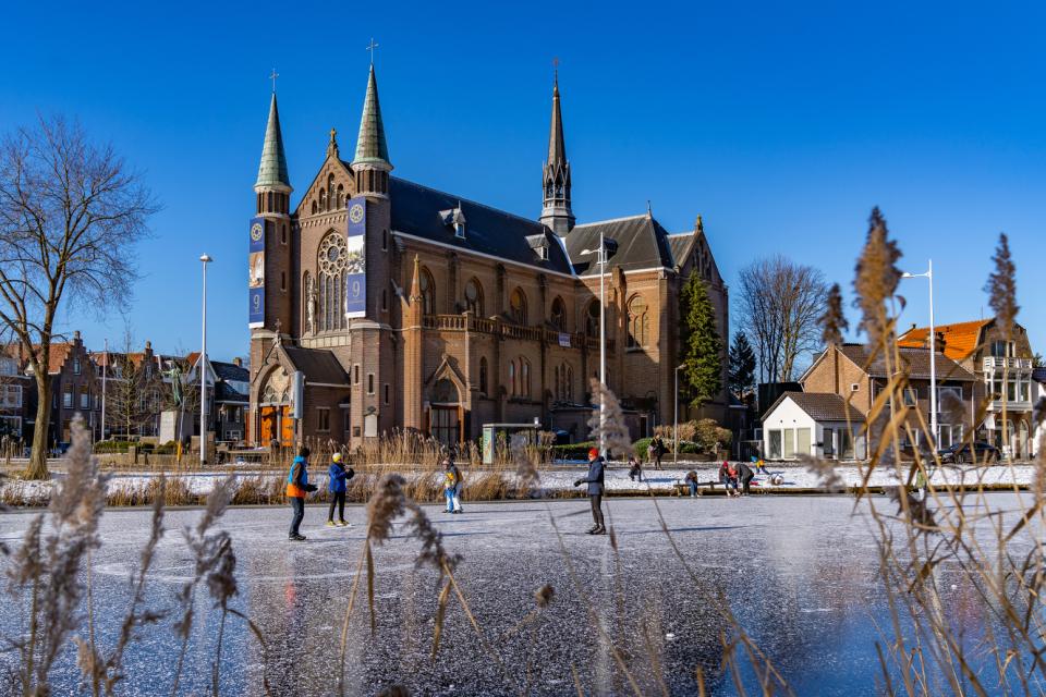 Singel bevroren met schaatsers op het ijs met op de achtergrond een kerk