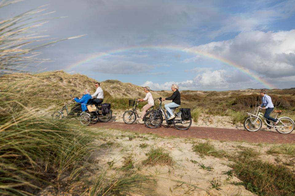 Fietsers door de duinen met een regenboog op de achtergrond