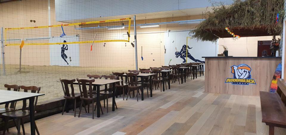 Binnen bij Indoor Beach alkmaar met beach volleybal veld en tafels met stoelen