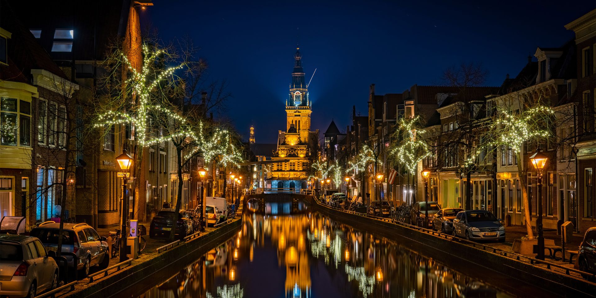 De waagtoren in het donker met kersversiering in de bomen